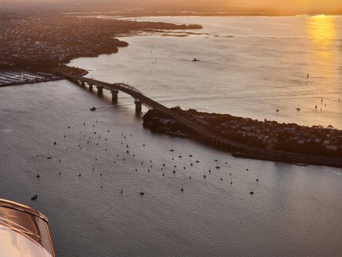 Aerial view at sunset of the Auckland Harbour Bridge over the Waitematā, moored yachts below, part of the aircraft in the corner
