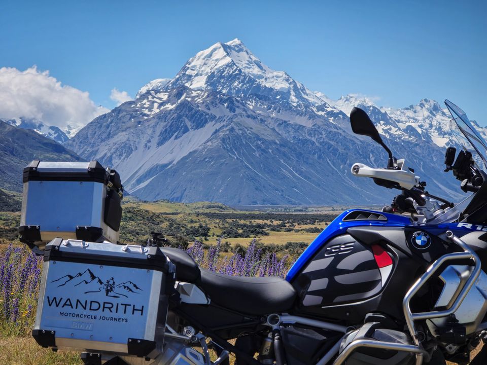 BMW GS Adventure with Wandrith panniers, purple wildflowers, and snow-covered Aoraki / Mount Cook under a blue sky