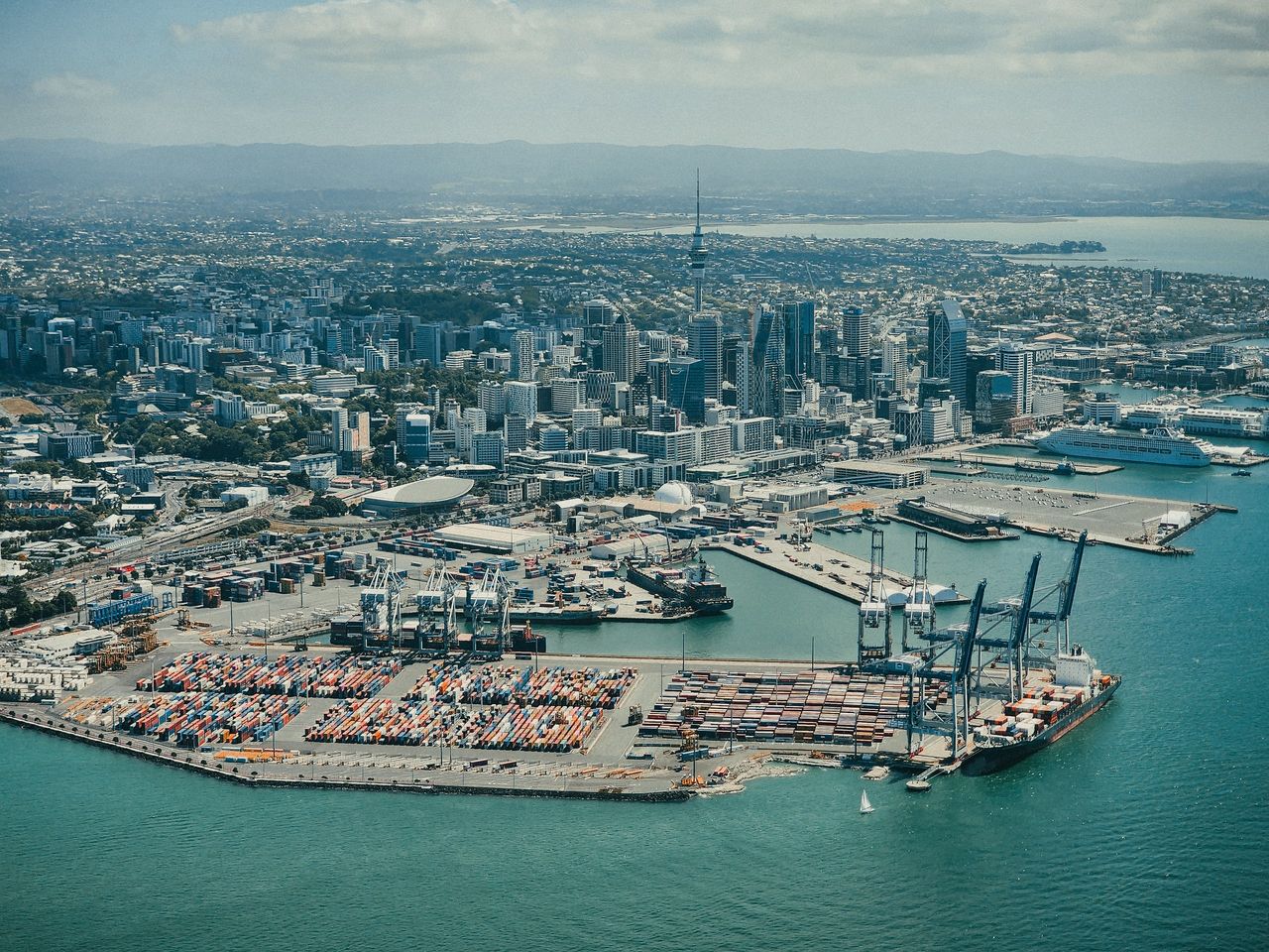 Aerial view of central Auckland's high-rises and Sky Tower above the container port, a moored cruise ship and the Waitematā Harbour