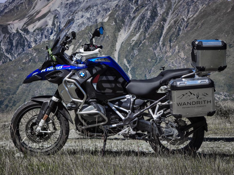 Side view of a blue, white and black BMW R1250GS Adventure with Wandrith panniers and top box, below a steep, scree-streaked mountainside