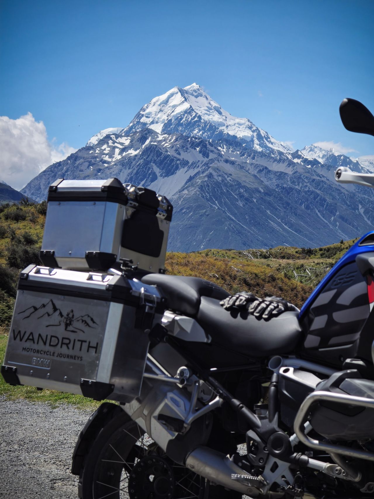 Snow-covered Aoraki / Mount Cook under blue sky behind a BMW adventure motorcycle, gloves on the seat, Wandrith pannier and top box