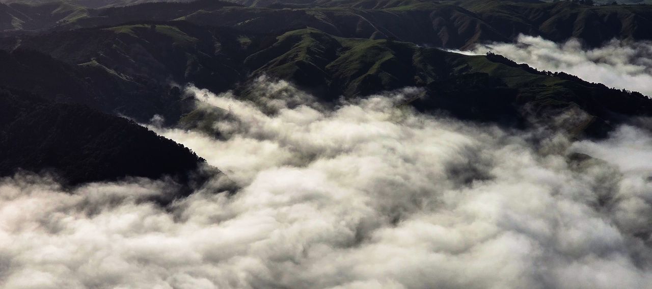 Aerial view of dark green hills and ridges with thick white fog filling the valleys between them