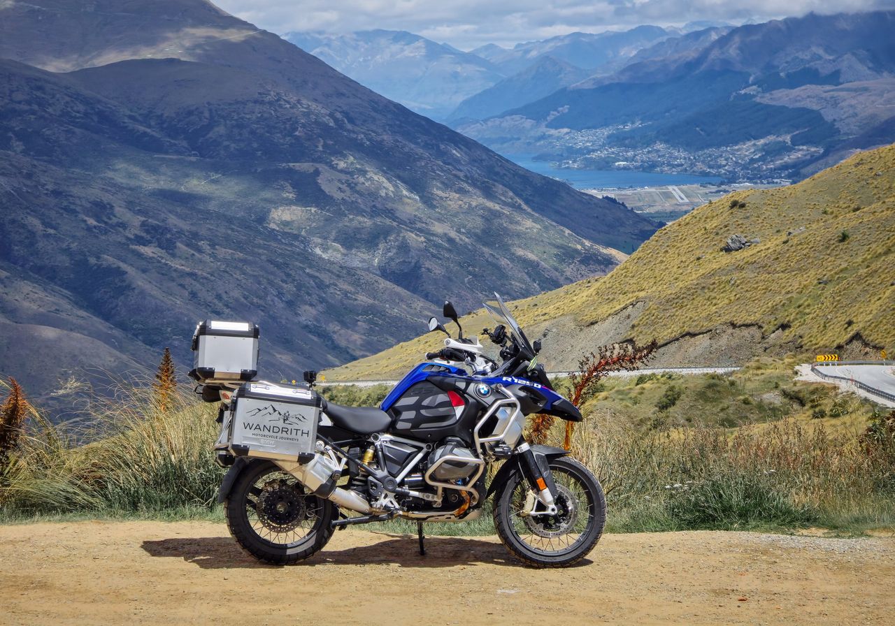 Blue and white BMW R 1250 GS Adventure with Wandrith panniers on a tussock hillside, looking down to Lake Wakatipu and Queenstown