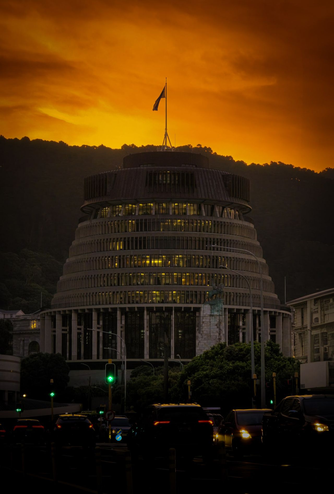 Wellington's round, tiered Beehive building against a fiery orange sky, a flag on its roof and car headlights on the street below